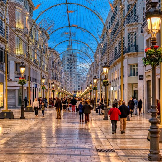 People walk and shop in pedestrian Larios street retail shops in downtown Malaga during Christmas holiday season, at dusk.
