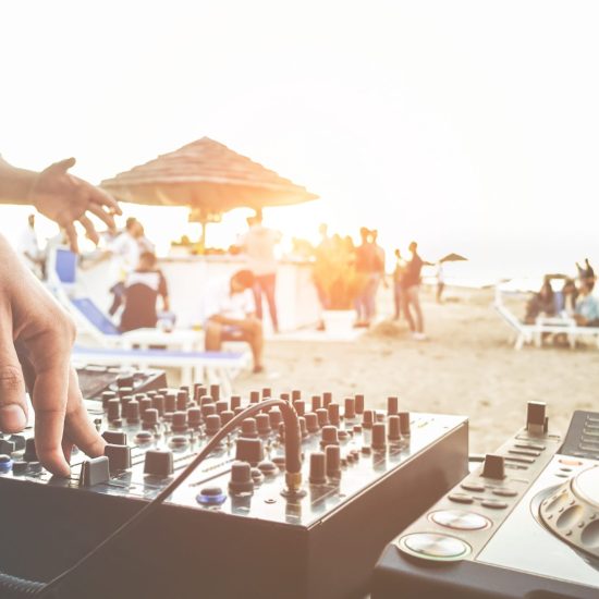 Dj mixing at sunset beach party in summer vacation outdoor - Disc jockey hands playing music for tourist people in chiringuito kiosk bar - Event, music and fun concept - Focus on right hand