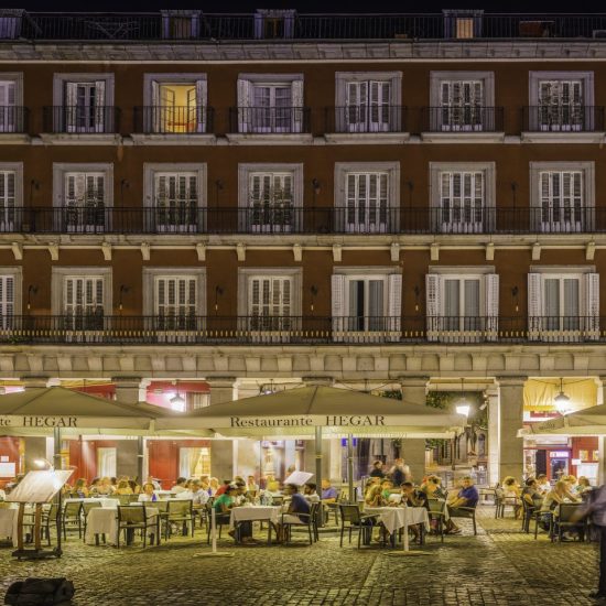 People eating and drinking at the al fresco tables of the restaurants and bars of the iconic Plaza Mayor illuminated by warm lamp light in the heart of Madrid, Spain's vibrant capital city. ProPhoto RGB profile for maximum color fidelity and gamut.